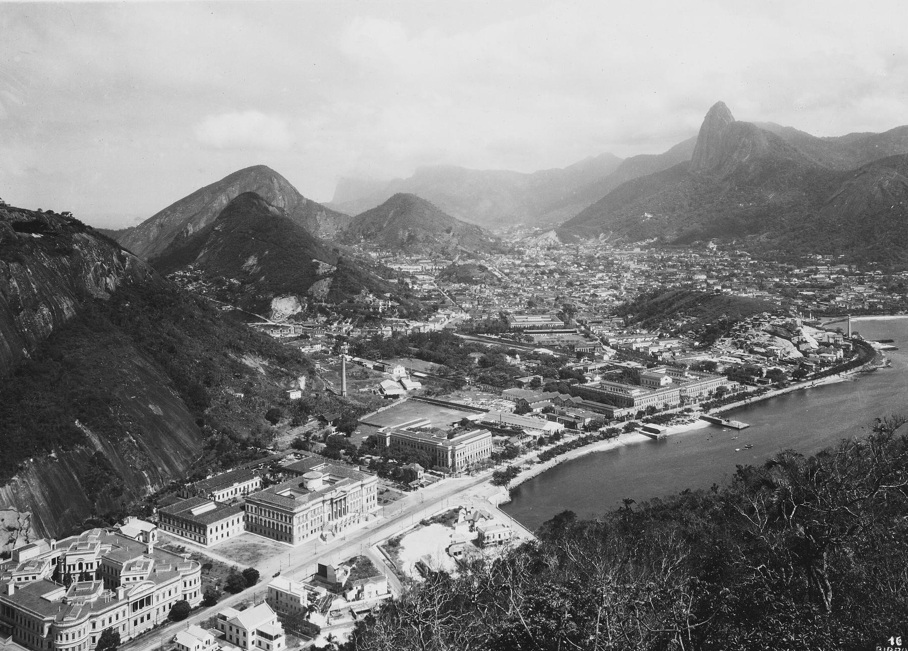 Enseada da Praia Vermelha vista do Morro da Urca, com o conjunto de edifícios institucionais à esquerda da praia — o IME entre eles — e Botafogo ao fundo.